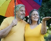 Senior couple enjoying monsoon under a colorful umbrella, reflecting comfort and safety in well-equipped senior living apartments during the rainy season.