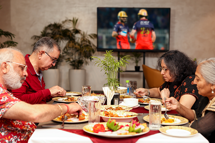 Family enjoying a delicious dinner together while watching cricket on TV | Saral Satya Legacy