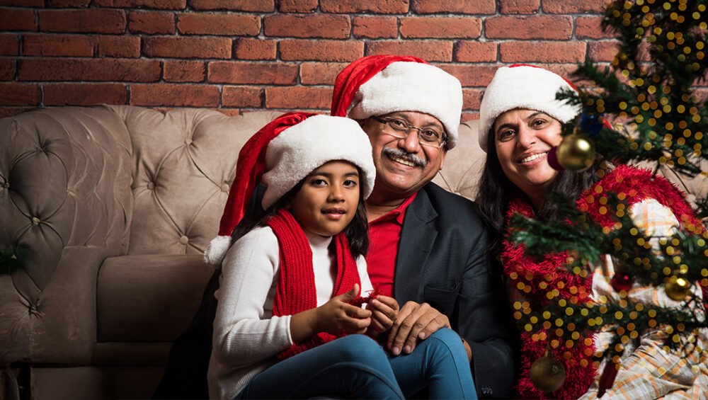 Smiling family wearing Santa hats sitting near a Christmas tree, highlighting festive social moments in retirement homes at Saral Satya Legacy.
