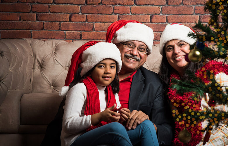 Smiling family wearing Santa hats sitting near a Christmas tree, highlighting festive social moments in retirement homes at Saral Satya Legacy.