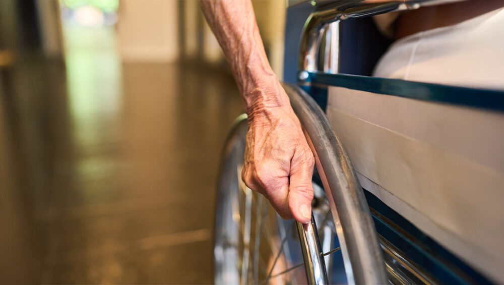 Close-up of a senior person’s hand on a wheelchair wheel, representing essential accessibility features in age-friendly senior homes at Saral Satya Legacy.