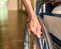 Close-up of a senior person’s hand on a wheelchair wheel, representing essential accessibility features in age-friendly senior homes at Saral Satya Legacy.
