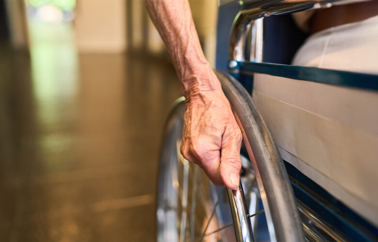 Close-up of a senior person’s hand on a wheelchair wheel, representing essential accessibility features in age-friendly senior homes at Saral Satya Legacy.
