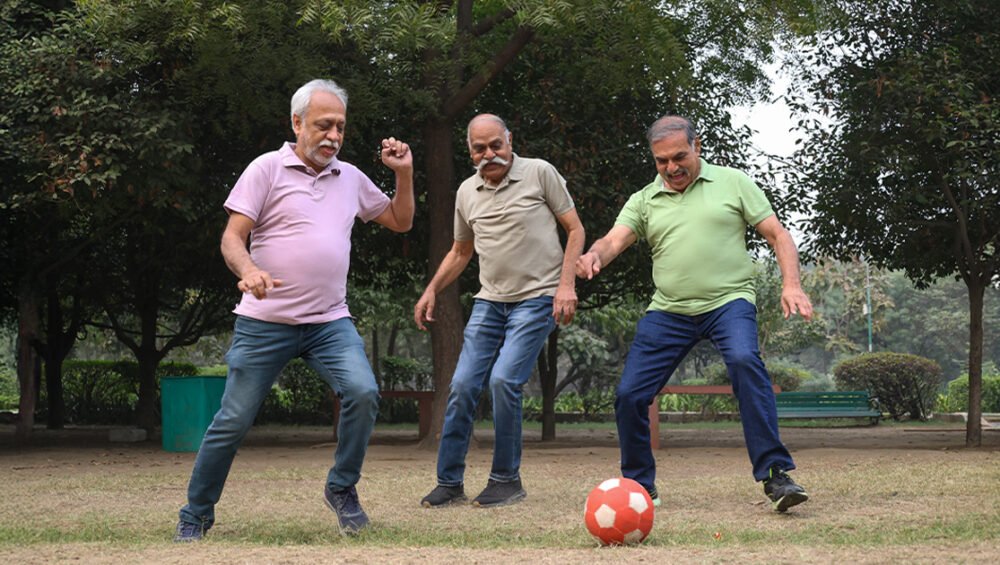 Three seniors playing football in a park, staying active and energetic—showcasing the importance of physical activity for seniors in retirement homes offered by Saral Satya Legacy.