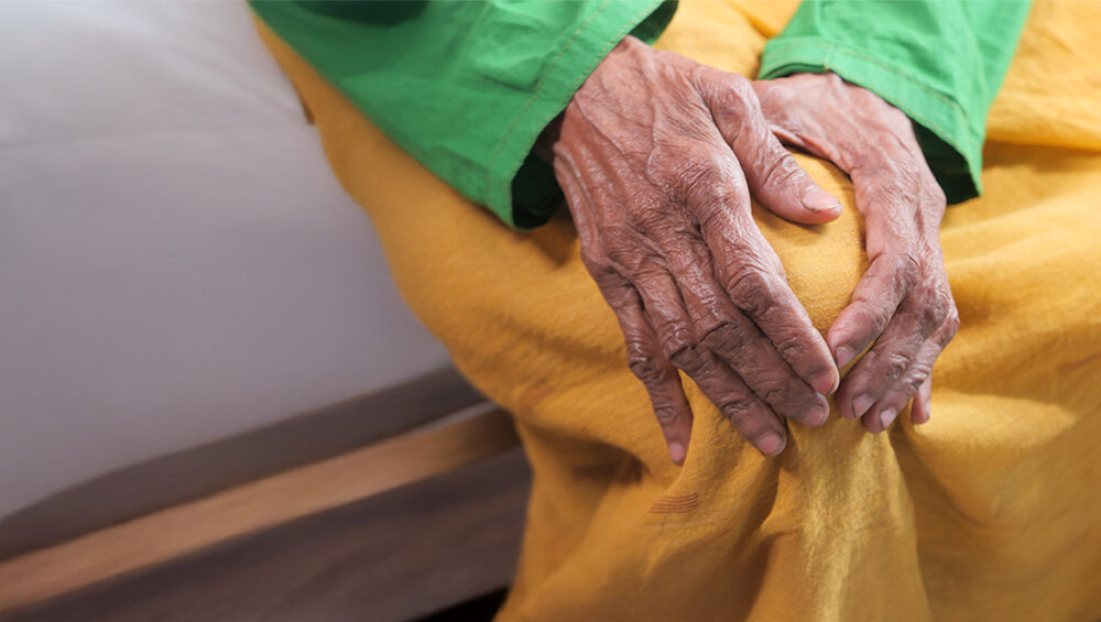 Close-up of an elderly person holding their knee, showing winter-related joint stiffness—Saral Satya Legacy.