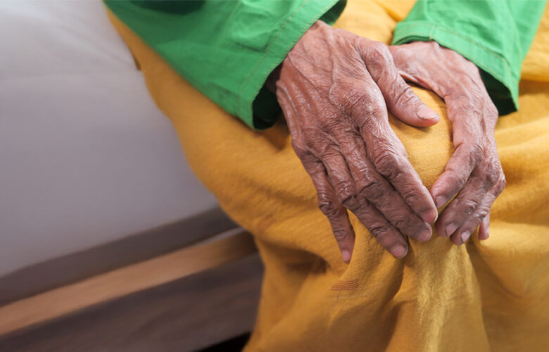 Close-up of an elderly person holding their knee, showing winter-related joint stiffness—Saral Satya Legacy.