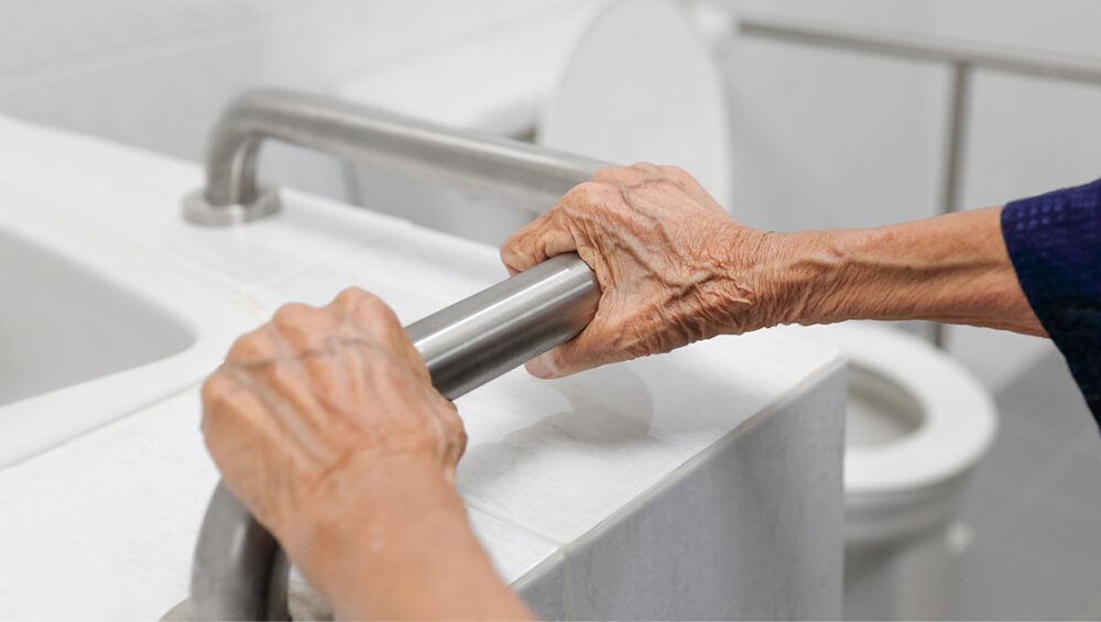 Senior citizen using a bathroom grab bar for support, highlighting safety features in retirement homes.