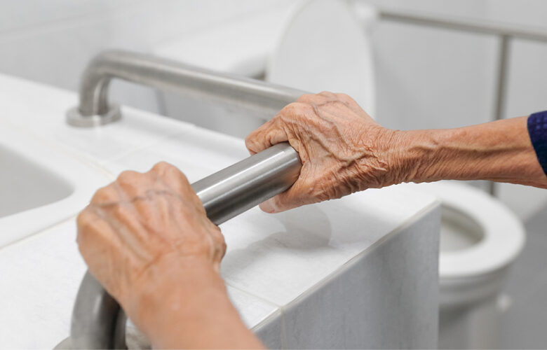 Senior citizen using a bathroom grab bar for support, highlighting safety features in retirement homes.