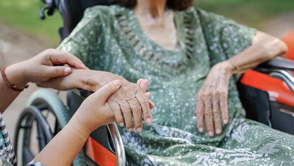 Caregiver holding the hand of a senior resident in a wheelchair at a luxury retirement home in Delhi NCR, reflecting personalized care and premium facilities by Saral Satya Legacy.