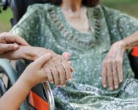 Caregiver holding the hand of a senior resident in a wheelchair at a luxury retirement home in Delhi NCR, reflecting personalized care and premium facilities by Saral Satya Legacy.